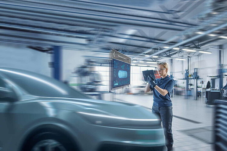 Mitarbeiterin in Kfz-Werkstatt liest Informationen zu Elekttroauto über Tablet aus.