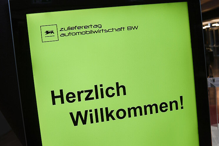 Gelbe Bildschirmanzeige, um die Teilnehmenden des Zulieferertags Automobilwirtschaft BW willkommen zu heißen.
