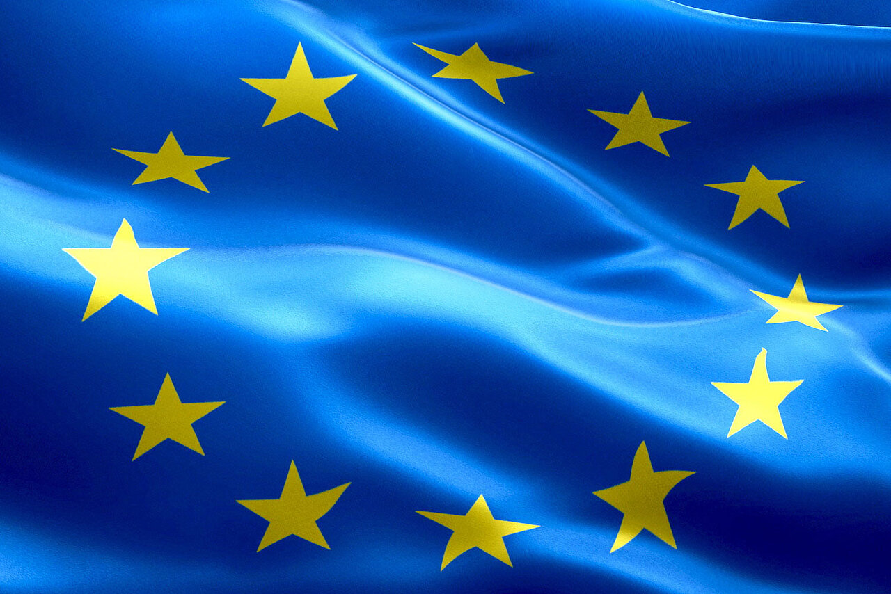 Wehende Flagge der Europäischen Union, blauer Hintergrund mit kreisförmig aufgestellten gelben Sternen.