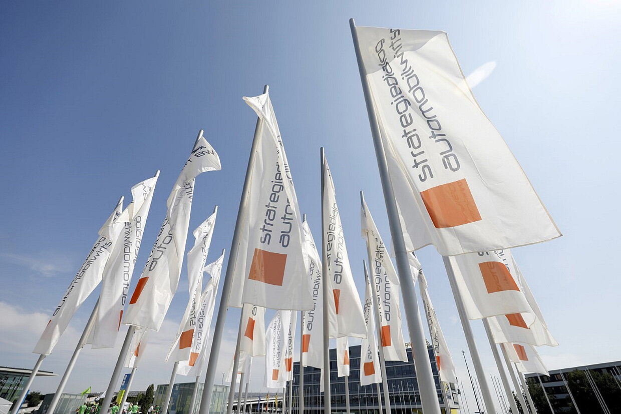 Strategiedialog Automobilwirtschaft BW Mehrere Fahren auf Messegelände, die das Logo des Strategiedialogs Automobilwirtschaft BW tragen.
