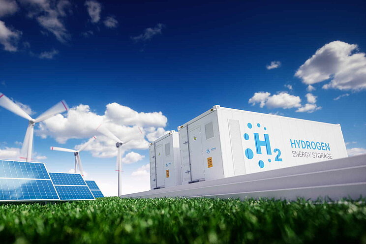 Windrad, Solaranlage und Elektrolyseur stehen nebeneinander auf einer grünen Wiese.
